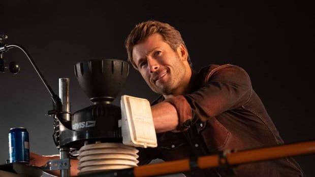 Glen Powell is seen smiling with blonde hair, leaning over equipment in the movie Twisters.