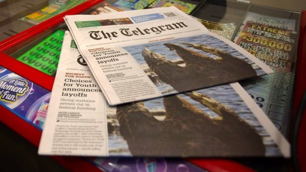 Two copies of a The Telegram newspaper lay on top of a glass countertop with scratch and win lottery tickets in a tray beneath. 