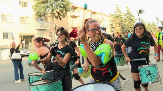 Drummers in green floaties play their instruments on the sidewalk as part of Festival des arts de ruelles