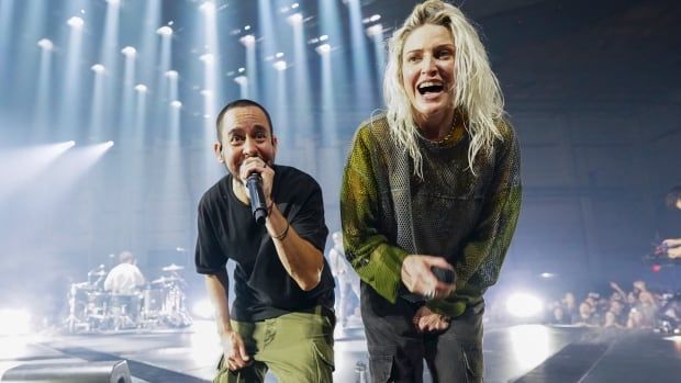 A man and a woman on stage look into a camera.