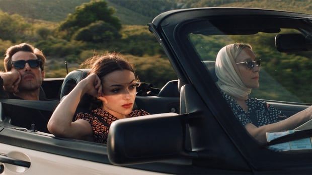 Three people sit in an open convertible.