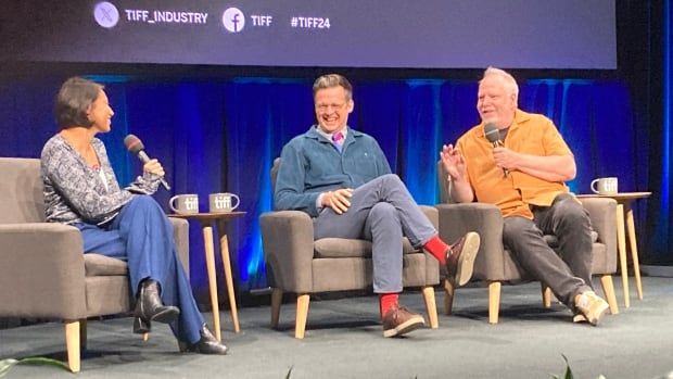 A woman and two men sit in armchairs on a stage.