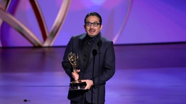 A person holds up an award while speaking into a microphone onstage.