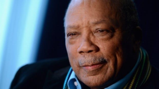 An older man, wearing a blue shirt, smiles.