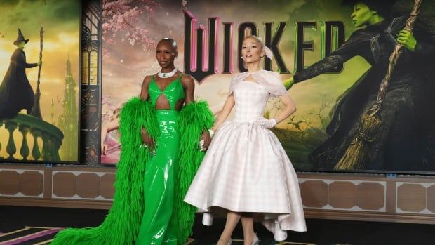 Two women, one in a green gown and one in a pink dress, are shown posing at a film premiere.