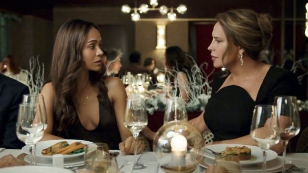 Two women in fancy outfits sit next to one another at a restaurant table. 