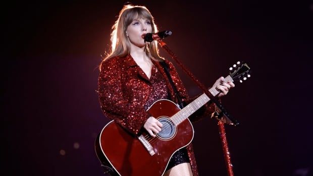 A woman in a glittering red jacket holds a red guitar while singing into a microphone. 