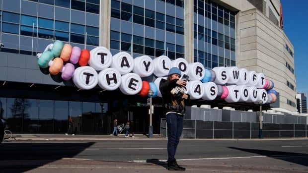 A woman takes a selfie in front of Rogers Centre stadium where hangs a giant friendship bracelet sign that reads: Taylor Swift The Eras Tour.