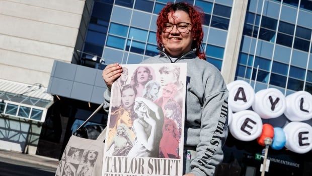 Holding a canvas bag on one shouldner, a woman shows off a poster that reads: Taylor Swift The Eras Tour, Toronto, Canada, outside Rogers Centre.