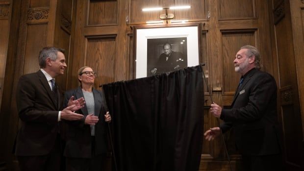 Three people stand next to a photo portrait unveiling.