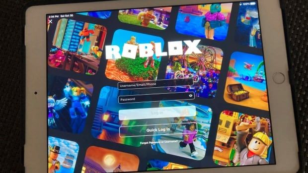 The log-in screen of Roblox is pictured on an iPad screen. It shows colourful images of Roblox gameplay behind the white Roblox title and the log-in prompts. 