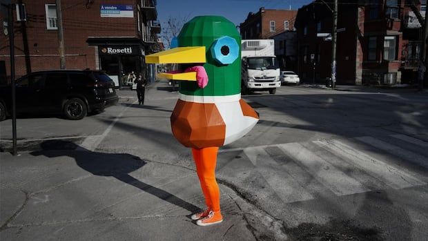 Lewis Mallard dressed in his duck costume with orange shoes and leggings stands on a Montreal sidewalk.