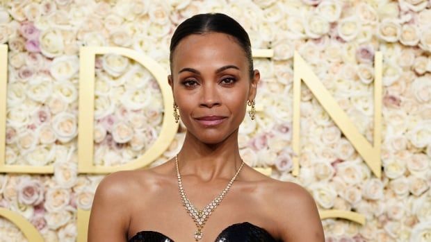 A woman stands in front of a gold backdrop.