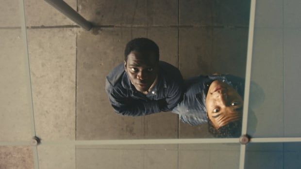 Two young men look up at their own reflections in a pane of glass. 