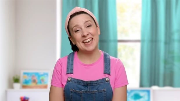 A smiling woman wearing a pink shirt, overalls and a pink headband. 