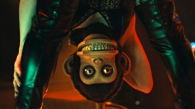 An upside down, grinning toy monkey is seen through someone's spread legs. 