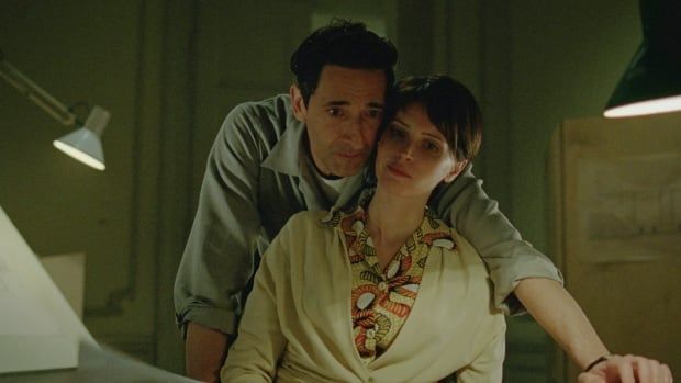 A man and a woman lean over a desk. 