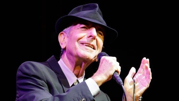 An older man wearing a suit and hat sings into a microphone. 