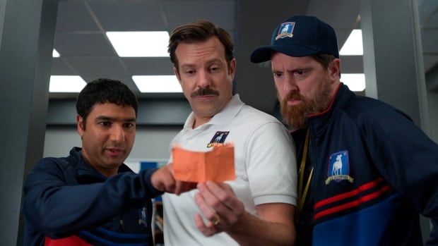 Three men read from an orange piece of paper.