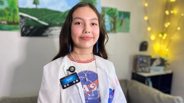 Young girl with her hair down, wears a light colored lab coat that she made that replicas a NASA lab coat.