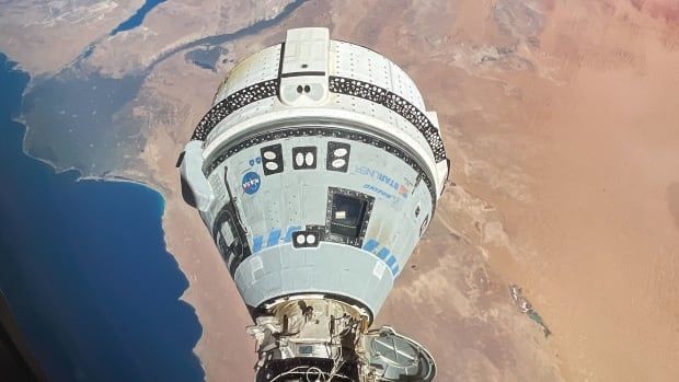 Earth is in the background with the ocean and desert, and in the foreground is a white spacecraft attached to the International Space Station.