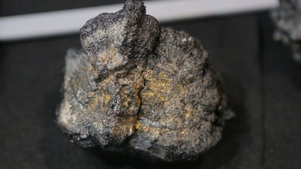 A lump of mineral with gold flecks sits on a black table