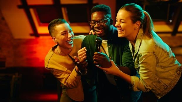 A stock image shows a man and two women smiling self-consciously and singing karaoke 