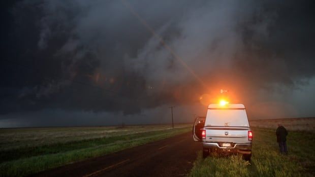 A truck pulled over next to a field with a dark storm in the background