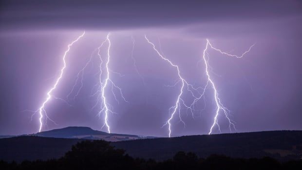 A purple sky with four lightning strikes hitting the ground. 