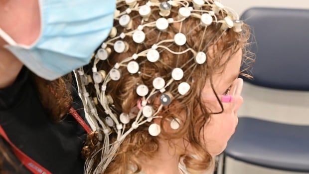 Girl wears an EEG cap and pink glasses in a lab.