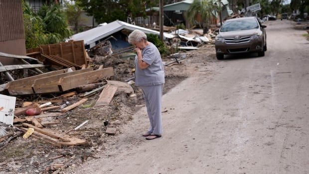 Woman with hand over mouth while looking at debris from destroyed house