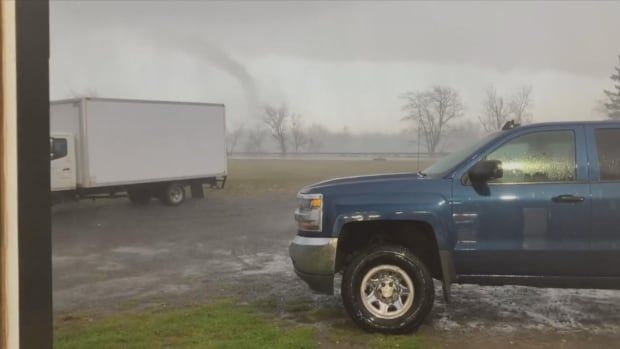 A tornado shown in the distance, a blue truck in the foreground.