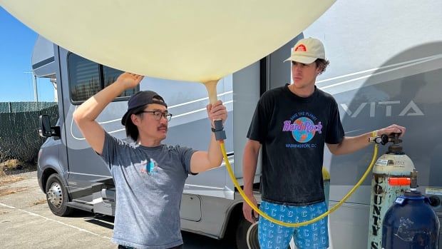 Two men fill a large balloon.