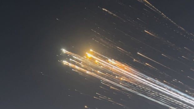 Streaks of orange and white light are seen against an evening sky.