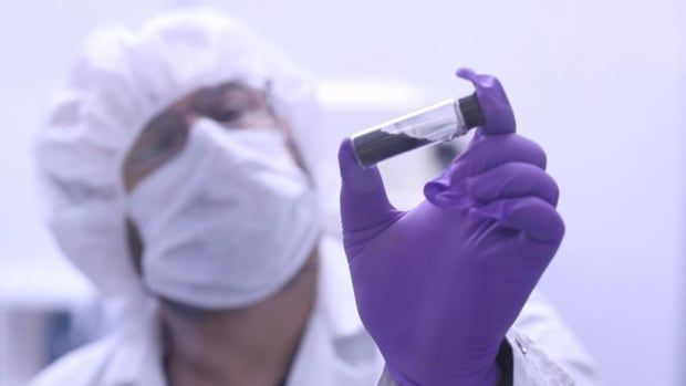 Man with purple glove holds up vial with black powder in it