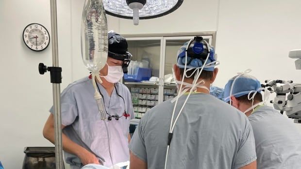 Three men in hospital smocks and masks stand over a patient in an operating room 