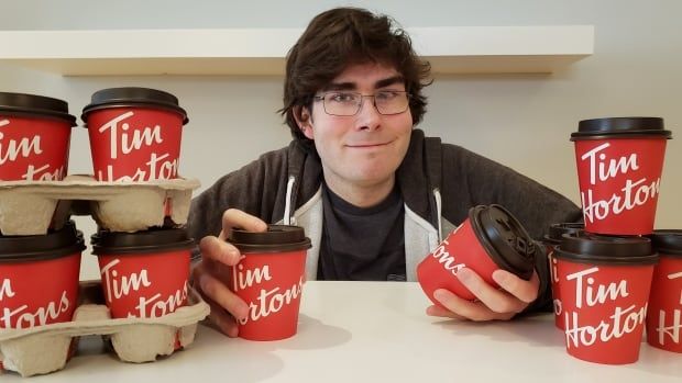 A man poses next to many, many Time Hortons coffee cups.