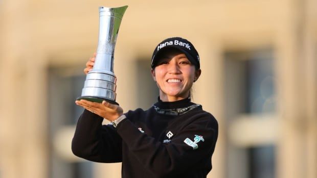 A woman golfer holds a trophy.