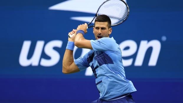 A male tennis player swings his racket with both hands to return a shot.