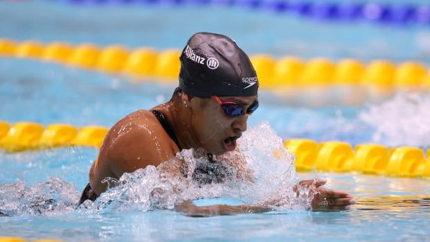 A female Para swimmer takes a large breath while racing in a breaststroke competition.