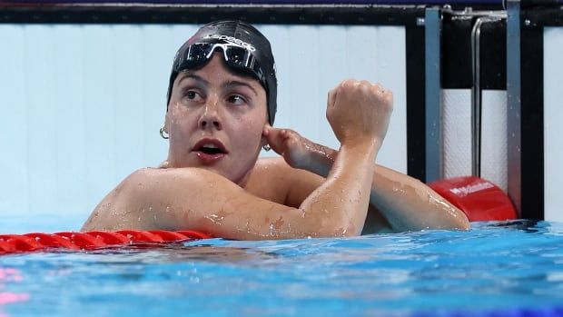 A female Para swimmer pumps her right fist in celebration while leaning on a lane divider inside a pool.