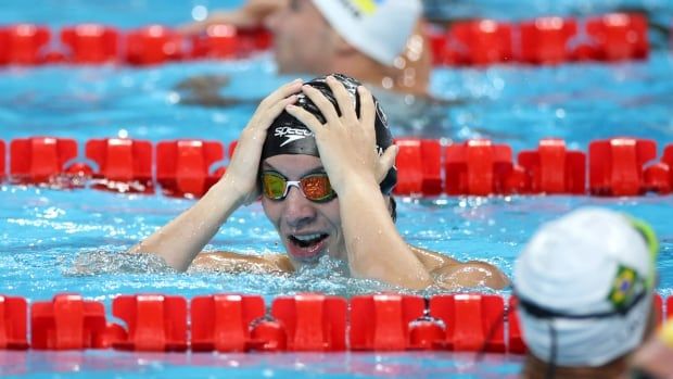 A swimmer puts his hands on his head.