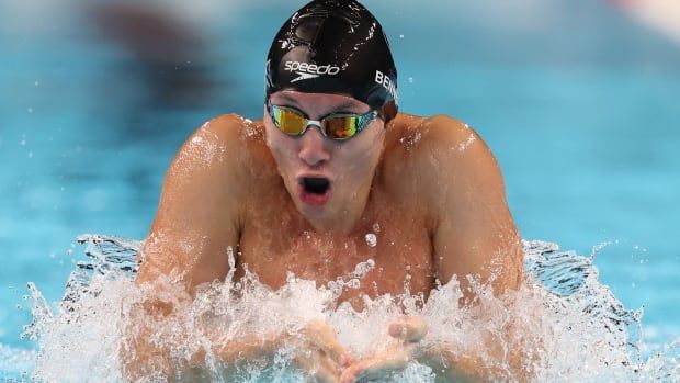 A male swimmer takes a deep breath as he competes in a breaststroke race.