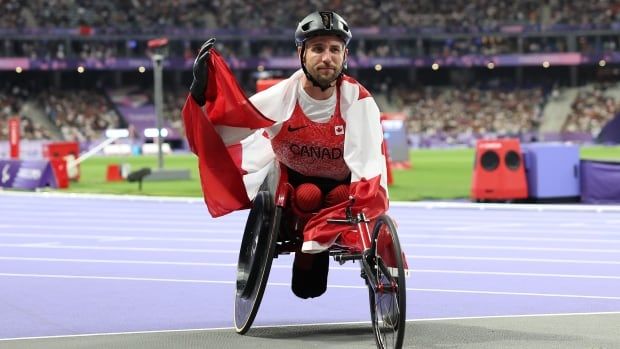 A man in a wheelchair poses with a Canadian flag draped over him.