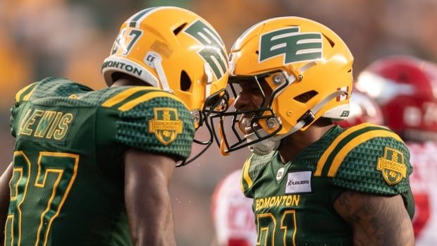 Two football players in green-and-yellow uniforms tap helmets in celebration on the field.