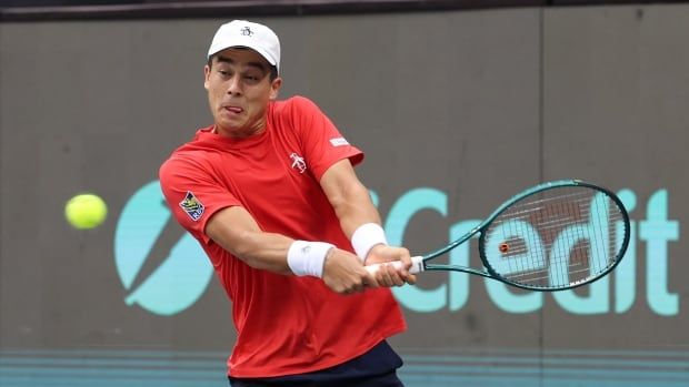 A men's tennis player aims a backhand shot.