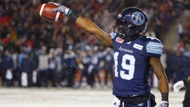 A male football receiver wearing number 19 holds a ball forward with his right hand to signal a first down during a game on a snowy field.