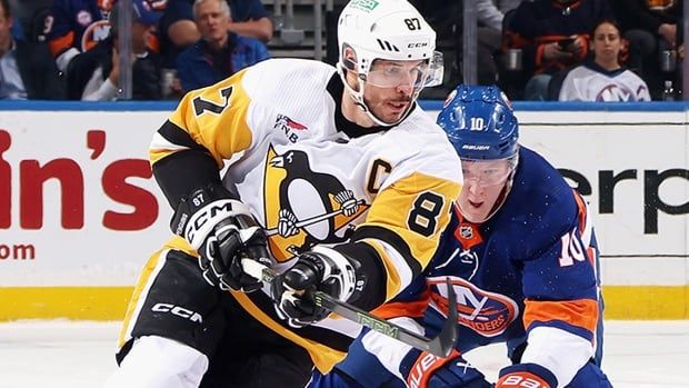 Pittsburgh Penguins captain Sidney Crosby tries to avoid a check from the New York Islanders' Simon Holmstrom during an April 17, 2024 NHL regular-season game in Elmont, New York.