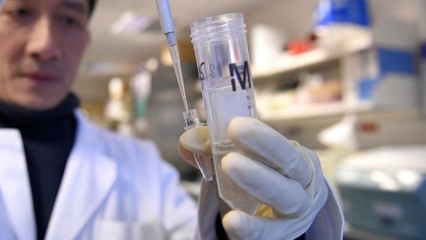 A man in a white lab coat and white latex gloves holds a test tube