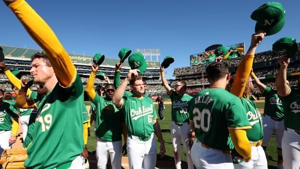 A group of male baseball players raise their hats to salute the crowd from the field.